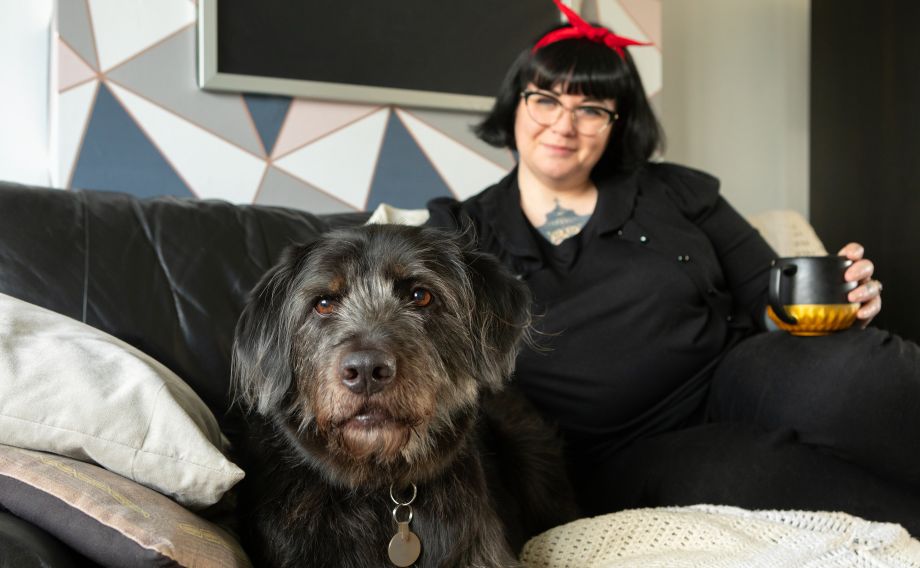 Lady sat on the sofa with a hot drink with a shaggy black dog